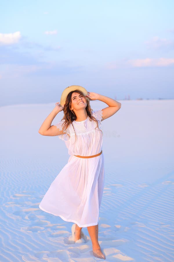 Young girl wearing dress and hat standing on white sand in blue