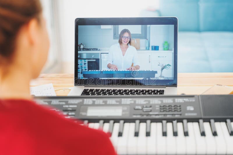 Young girl woman learns to play the piano with a teacher on a video conference from a laptop. The teacher on the screen explains