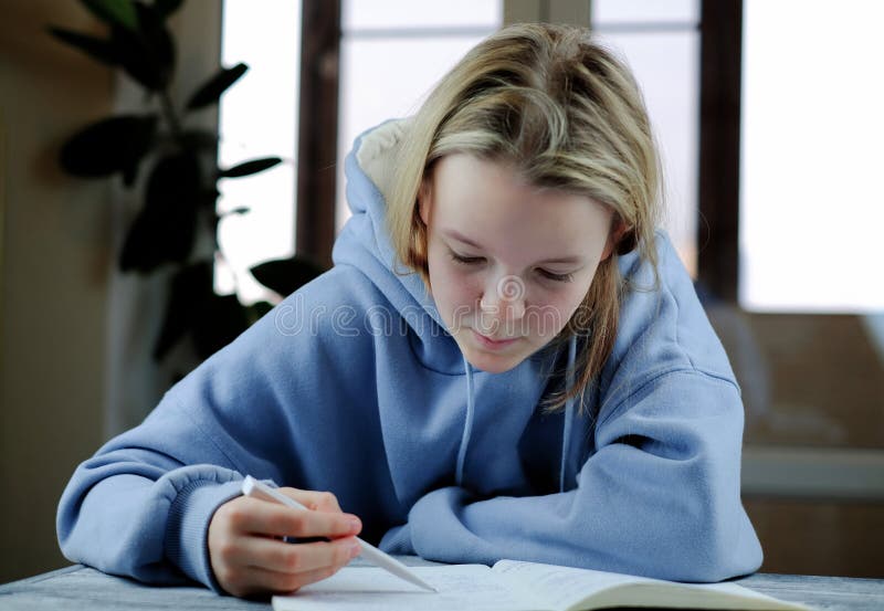 Young girl writing task with pen in copybook, studing at home