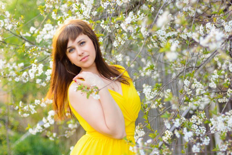 Young girl in yellow dress in spring on cherry blossom