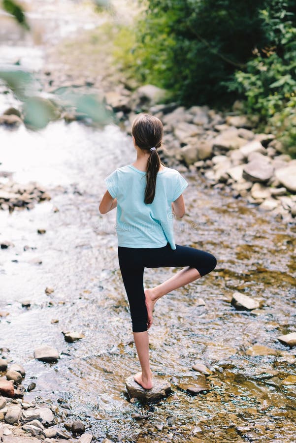 Young girl yoga meditating at sunrise standing on stones on the shore of a mountain stream. Teenage model meditating in peaceful stock image Young girl yoga meditating at sunrise standing on stones on the shore of a mountain stream. Teenage model meditating in peaceful stock image