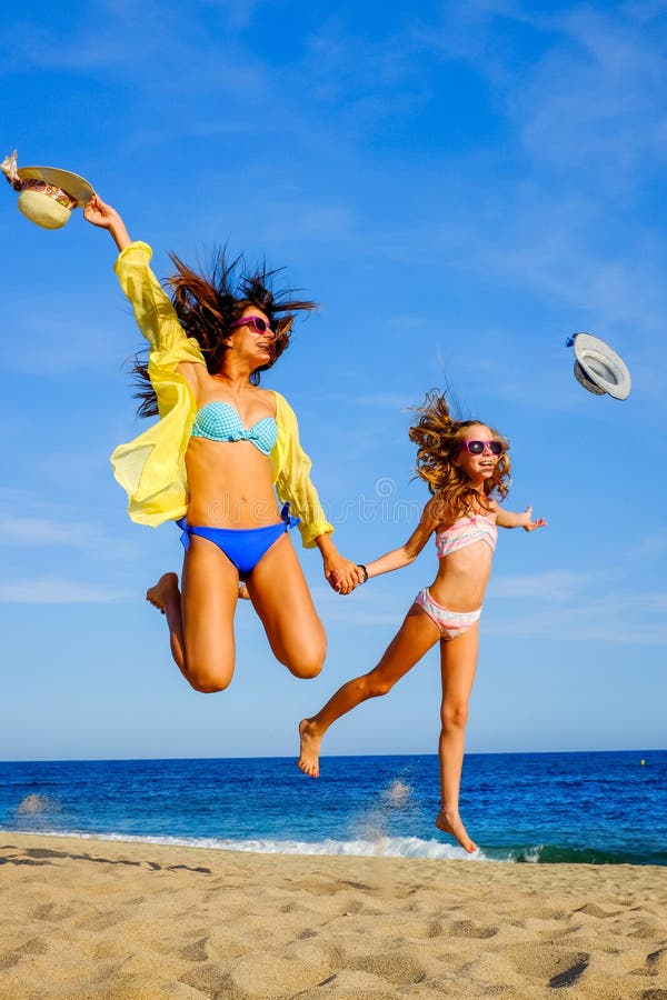 Young girls in swimwear jumping on beach.