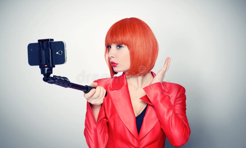 Young glamor girl in red making selfie with a stick