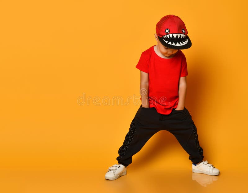 Young guy boy in a red T-shirt and dark pants, white sneakers and a funny cap posing on a free copy space on a yellow background