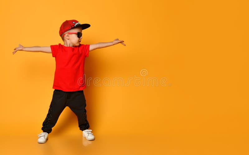 Young guy boy in a red T-shirt and dark pants, white sneakers and a funny cap posing on a free copy space on a yellow background