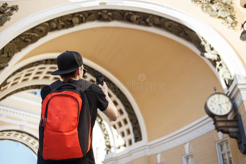 Young guy tourist with backpack photographing historical arch of General Staff Building in the palace square in St