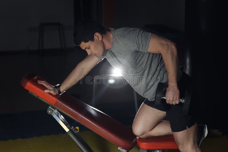 Young handsome adult male doing one-arm dumbbell rows on bench in modern gym. royalty free stock image Young handsome adult male doing one-arm dumbbell rows on bench in modern gym. royalty free stock image
