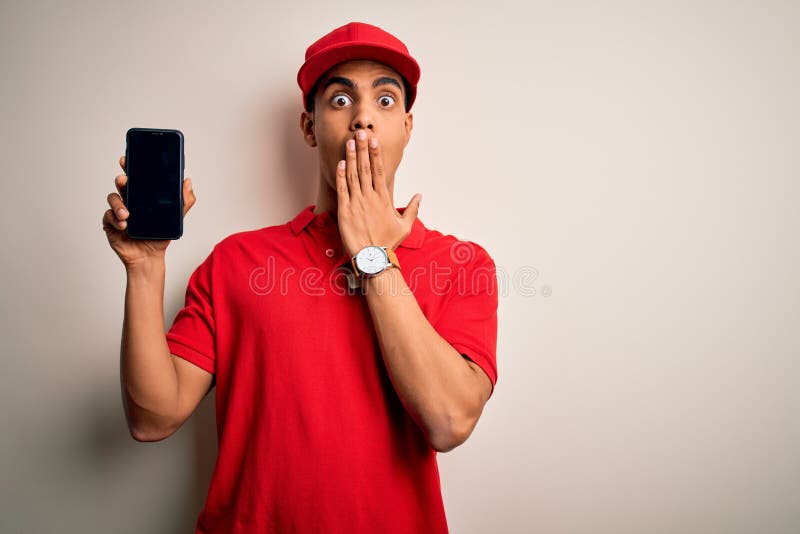 Young handsome african american delivery man holding smartphone showing screen app cover mouth with hand shocked with shame for