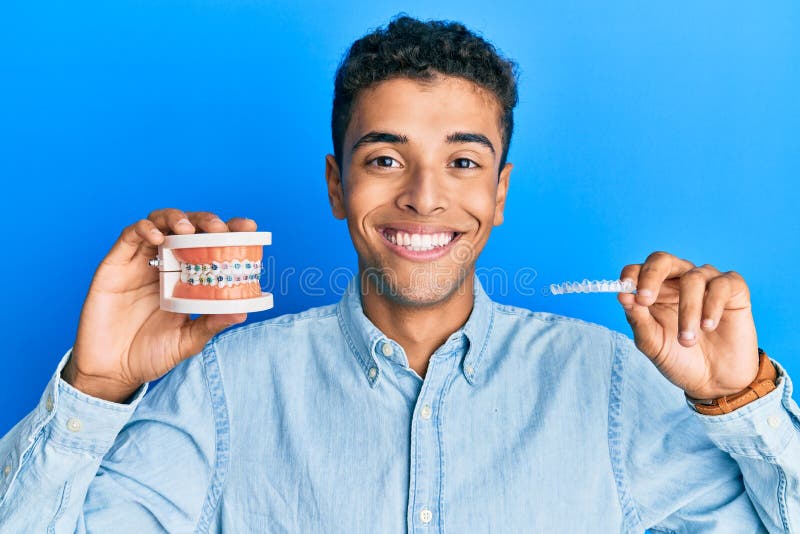 Young handsome african american man holding invisible aligner orthodontic and braces smiling with a happy and cool smile on face