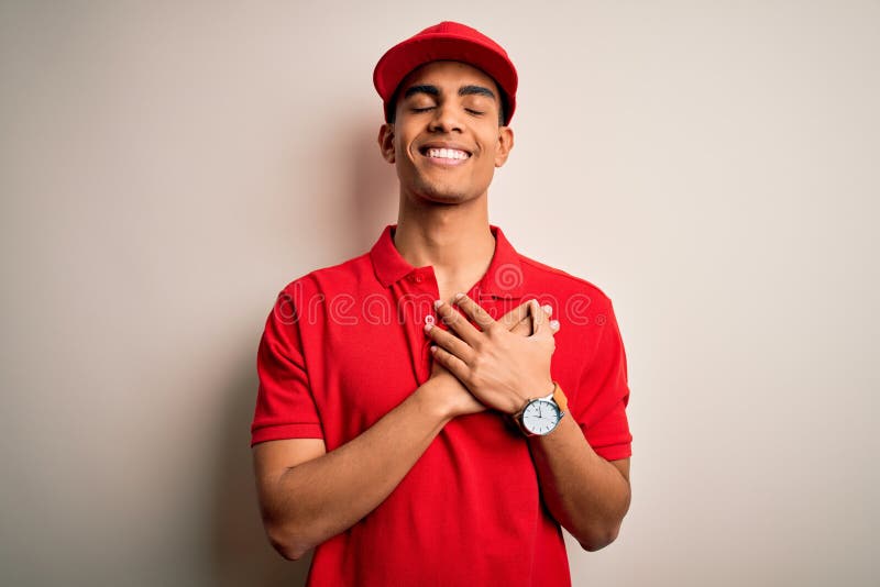 Young handsome african american man wearing casual polo and cap over red background smiling with hands on chest with closed eyes
