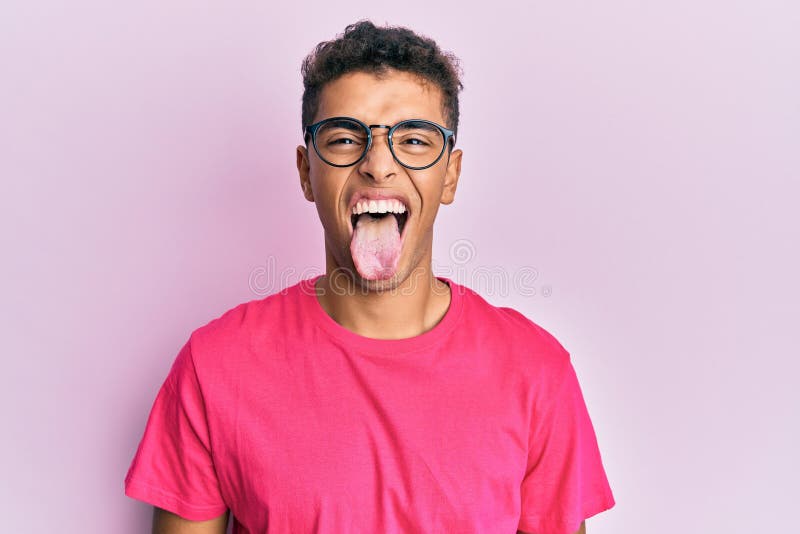 Young handsome african american man wearing glasses over pink background sticking tongue out happy with funny expression