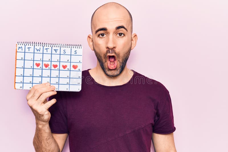 Young Handsome Bald Man Holding Heart Calendar Scared and Amazed with