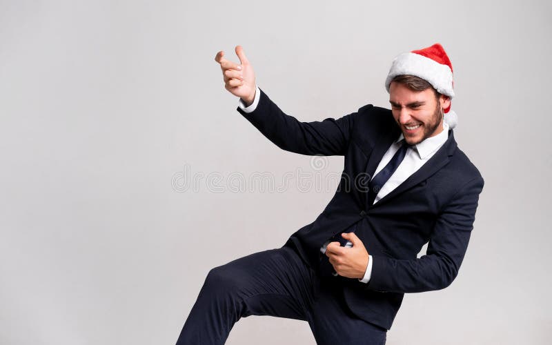 Young handsome caucasian guy in business suit and Santa hats stands on white background in studio and Plays on an imaginary guitar