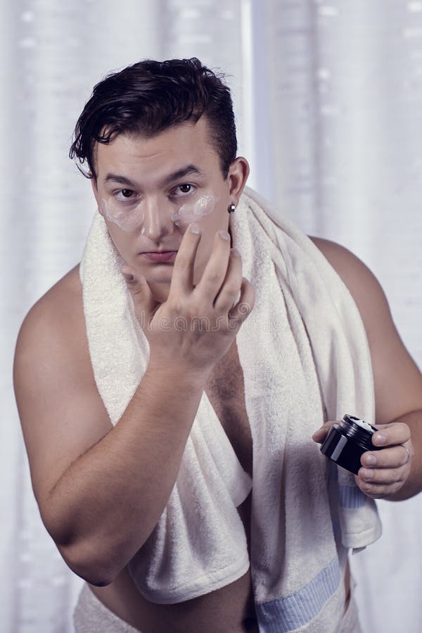 Young handsome caucasian man applying cream under the eyes, towel on shoulders. Caring face, metrosexual daily routine in the bath royalty free stock photography Young handsome caucasian man applying cream under the eyes, towel on shoulders. Caring face, metrosexual daily routine in the bath royalty free stock photography