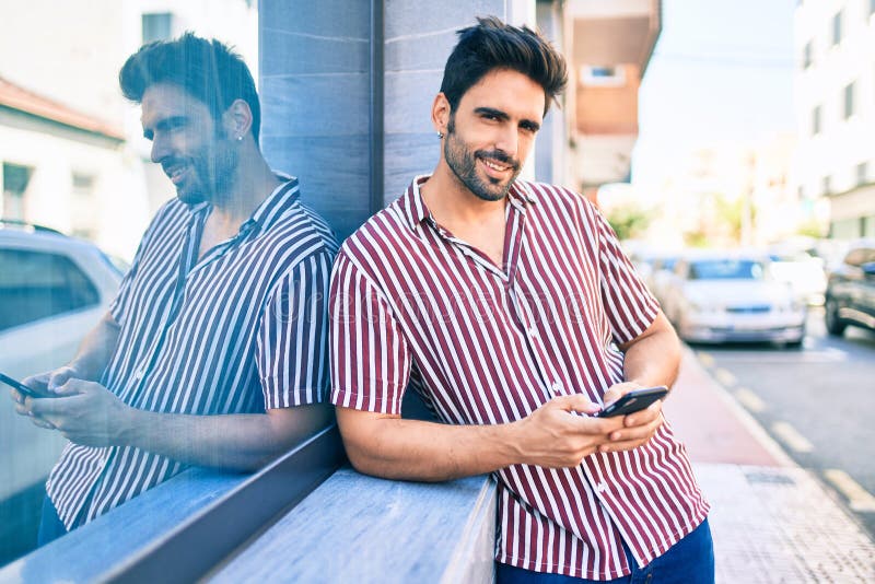 Young handsome hispanic man with beard smiling happy outdoors using smartphone royalty free stock photos