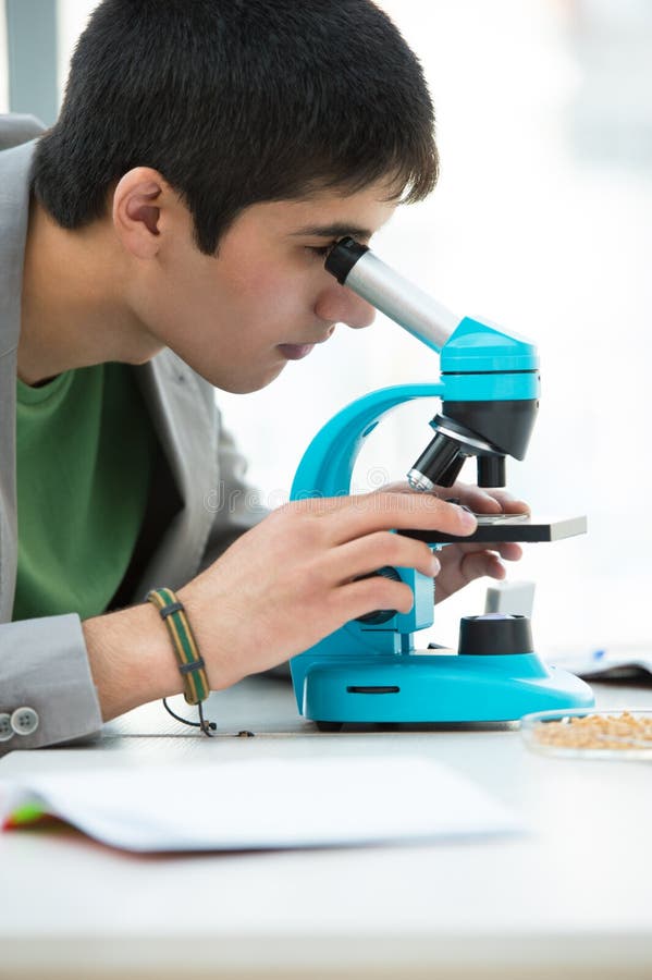 Young handsome male student peering through microscope