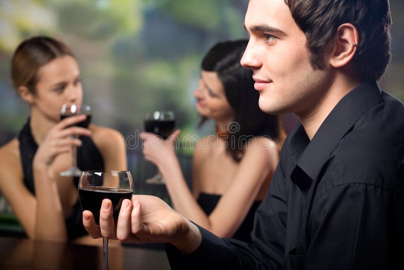 Young handsome man with glass of red-wine and two women stock photography Young handsome man with glass of red-wine and two women stock photography