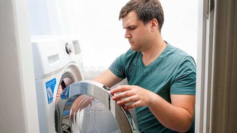 Young handsome man loading dirty clothes in washing machine and doing laundry. Male housework and daily routine at home. Automatic loading stock images, royalty-free photos and pictures