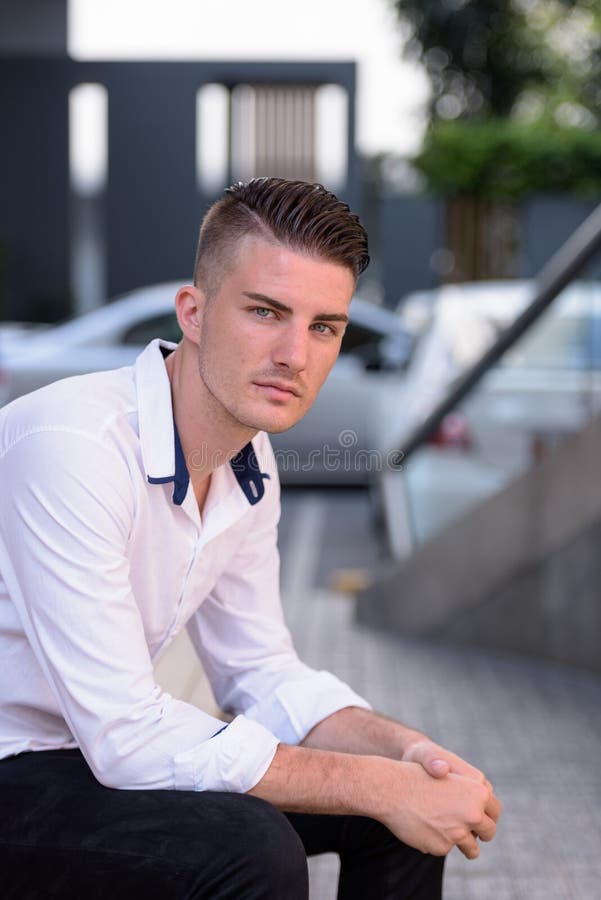 Young handsome man looking at camera while sitting outside moder royalty free stock photo Young handsome man looking at camera while sitting outside moder royalty free stock photo