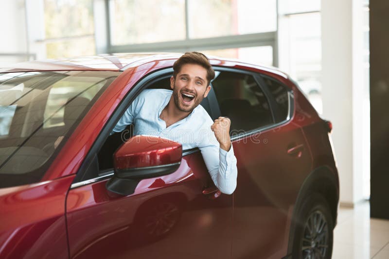 Young handsome man looking for new car in dealership center sticking out the vehicle window royalty free stock image Young handsome man looking for new car in dealership center sticking out the vehicle window royalty free stock image