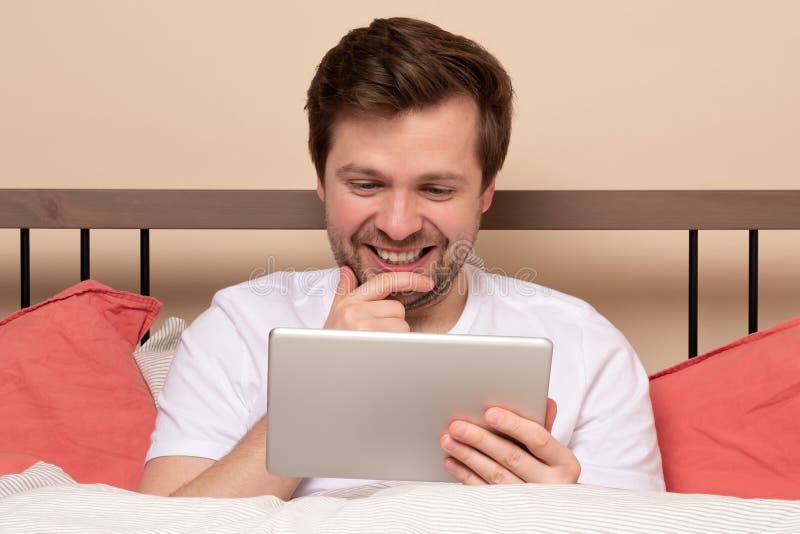 Young Handsome Man Lying In Bed And Using Tablet Computer Or Reading An Ebook Stock Image