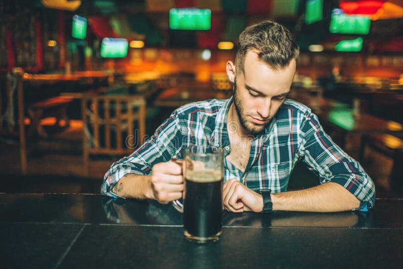 One Young Man Sit Alone at Bar Counter in Pub. he Hold Mug of Dark Beer ...