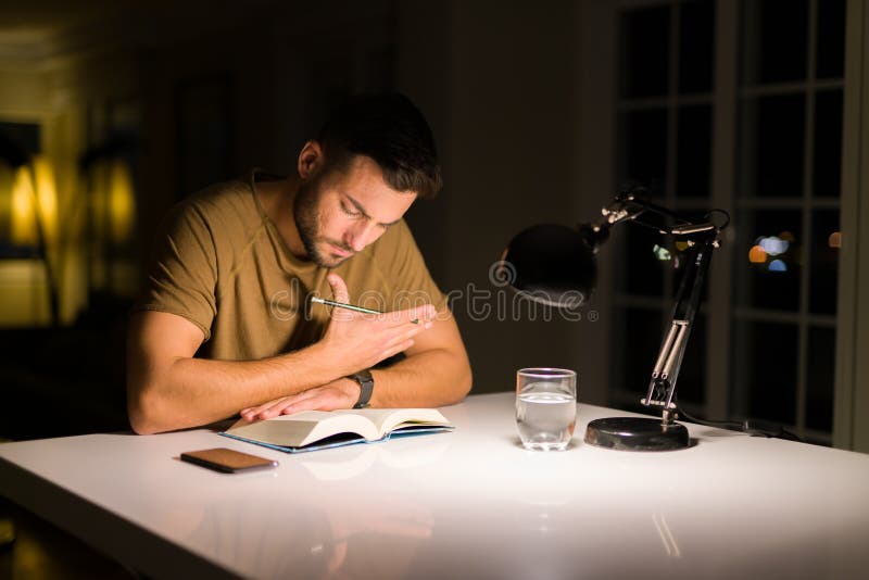 Young handsome man studying at home, reading a book at night stock photography