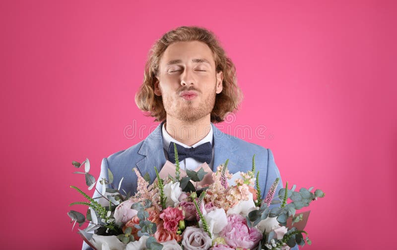 Young handsome man in  suit with beautiful flower bouquet on pink background