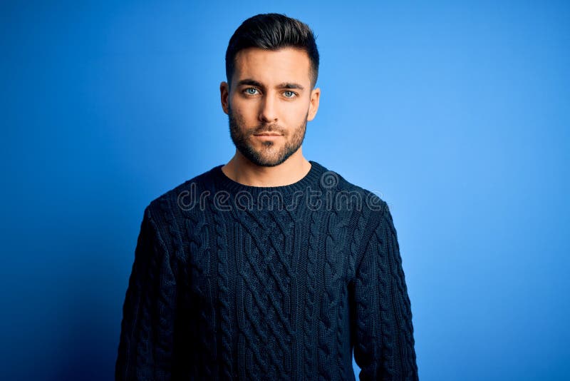 Young handsome man wearing casual sweater standing over isolated blue background Relaxed with serious expression on face