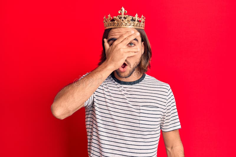 Young handsome man wearing prince crown peeking in shock covering face and eyes with hand, looking through fingers afraid royalty free stock photography