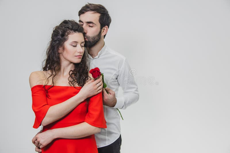 A young, handsome man gently covers his beautiful wife. During this time, one red rose. The girl is dressed in a red stock photography A young, handsome man gently covers his beautiful wife. During this time, one red rose. The girl is dressed in a red stock photography