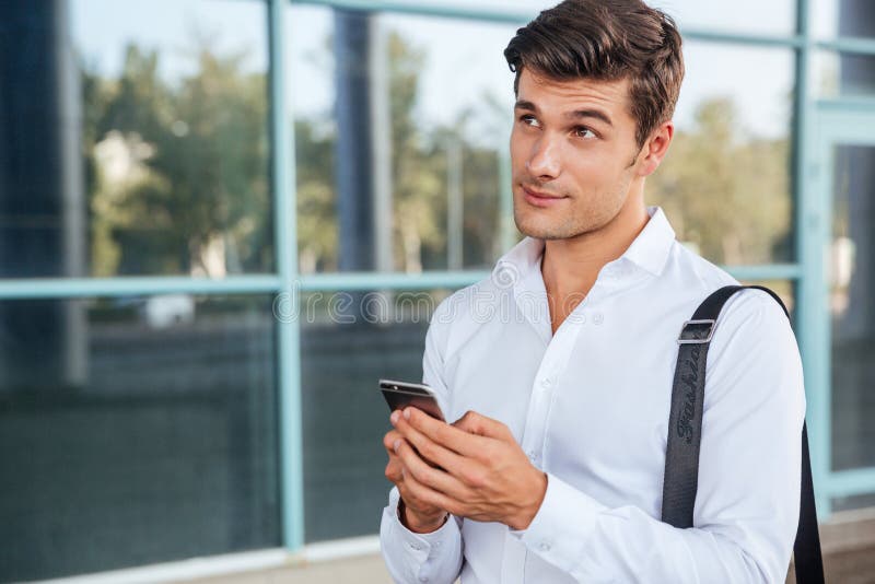 Young handsome pensive businessman using mobile phone outdoors