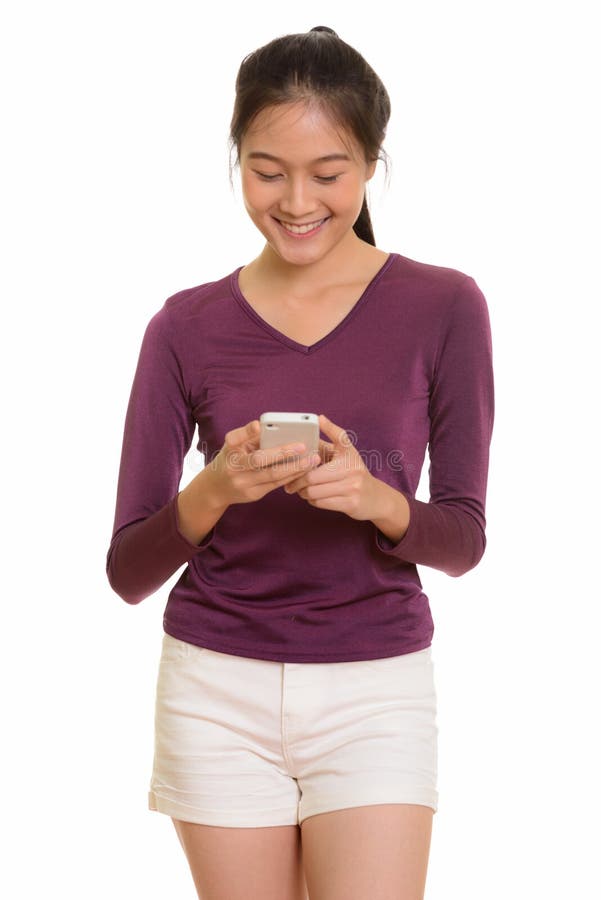 Young happy Asian teenage girl smiling and using mobile phone