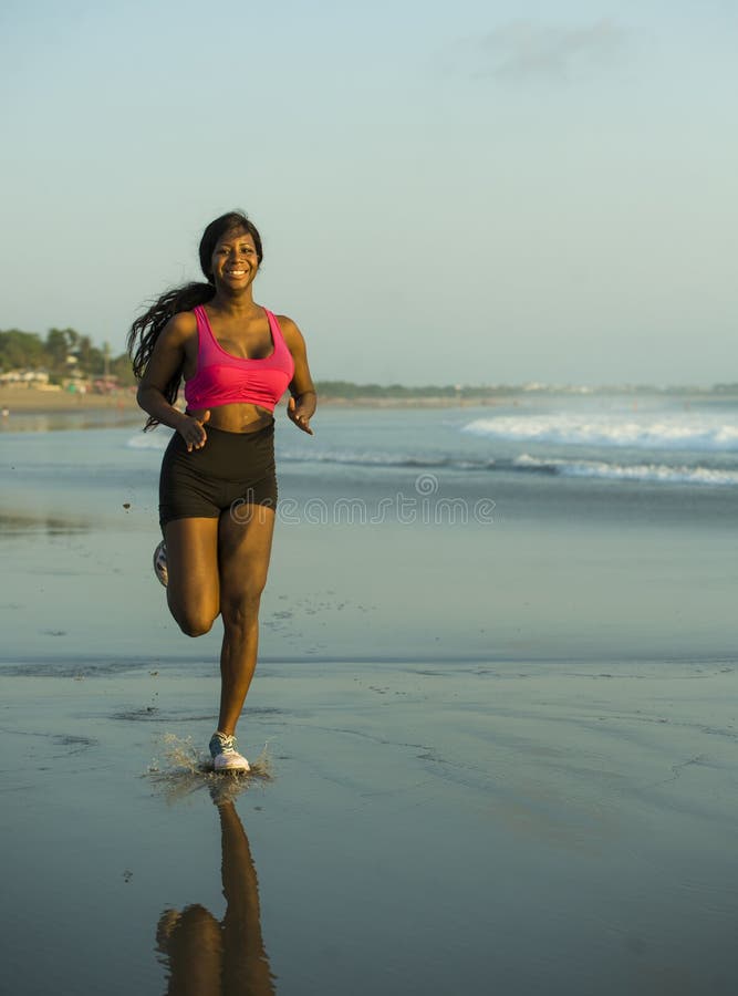 Young happy and attractive African American runner woman exercising on running workout at beautiful beach jogging and enjoying sun stock images Young happy and attractive African American runner woman exercising on running workout at beautiful beach jogging and enjoying sun stock images