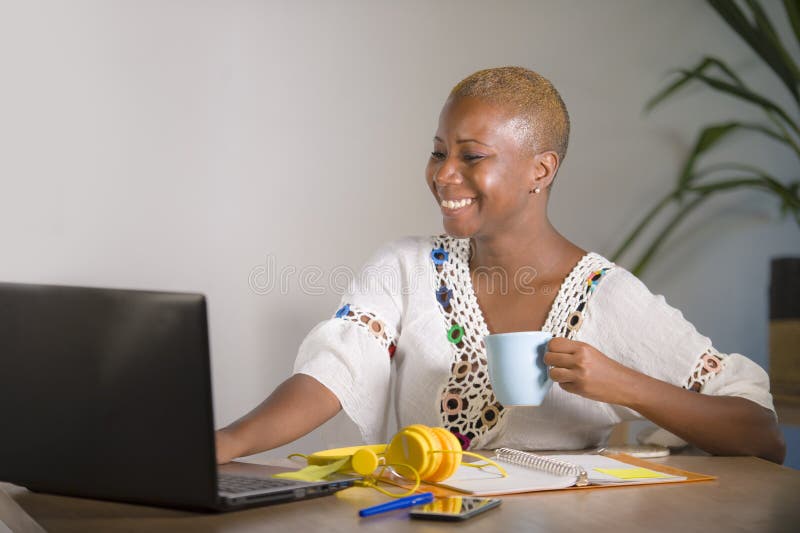 Young happy and attractive hipster black afro American woman drinking tea or coffee at home office working cheerful with laptop computer in digital nomad self-employed and internet job concept