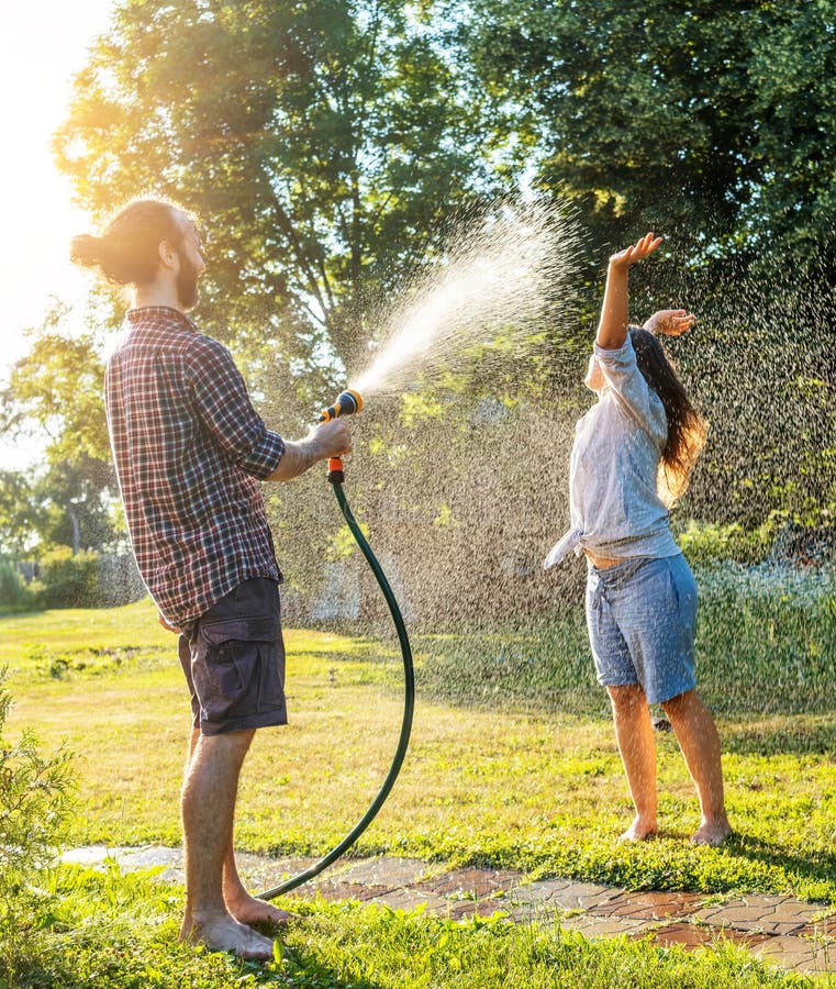 Young happy beautiful couple hosing in the garden, summer happiness and love concept, poured water from a garden hose of a spray