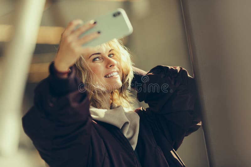 Young happy blonde in jacket makes selfie against background of window royalty free stock photos Young happy blonde in jacket makes selfie against background of window royalty free stock photos