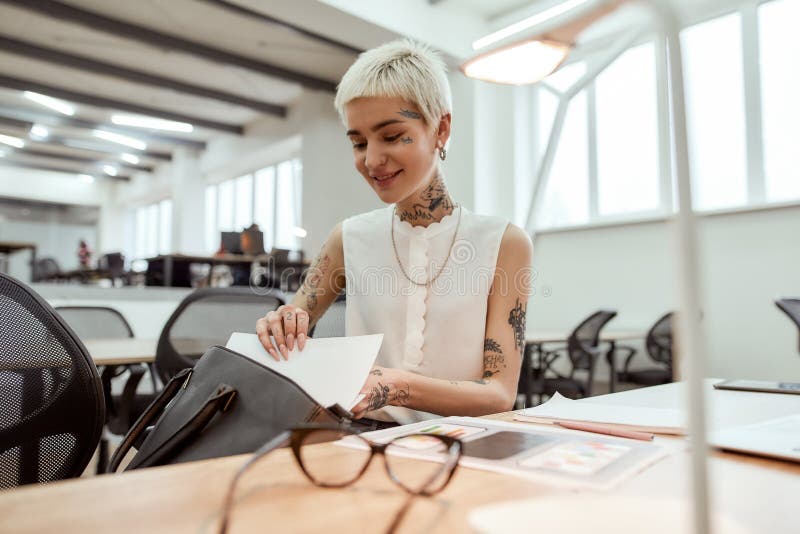 I found it. Young happy blonde tattooed businesswoman with short haircut taking out some documents from her handbag and