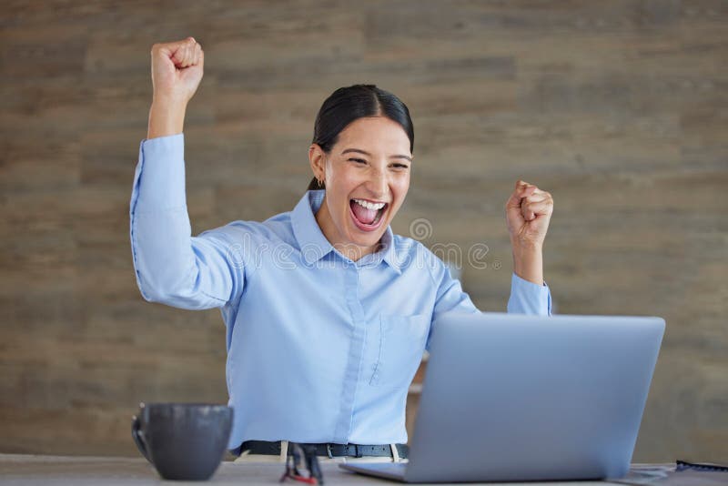 Young happy and excited mixed race businesswoman cheering with her fists working on a laptop sitting in an office at
