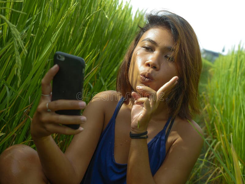 Young happy and exotic islander Asian girl from Indonesia taking selfie self portrait photo with mobile phone smiling cheerful and royalty free stock photography Young happy and exotic islander Asian girl from Indonesia taking selfie self portrait photo with mobile phone smiling cheerful and royalty free stock photography