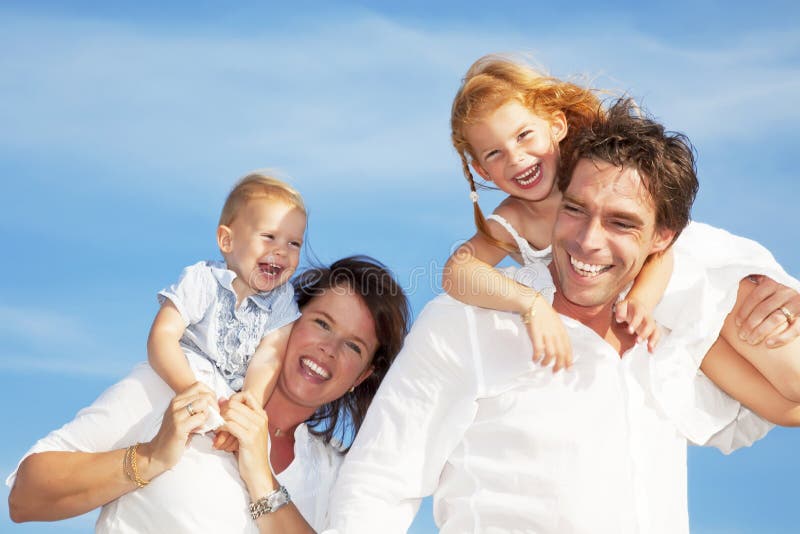 Giovane famiglia felice divertirsi all'aria aperta, vestita di bianco e con il cielo azzurro sullo sfondo.