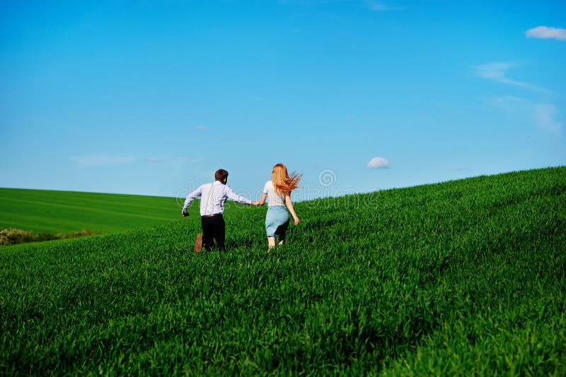 Young happy lovers running on meadow with green grass and blue s stock photography Young happy lovers running on meadow with green grass and blue s stock photography