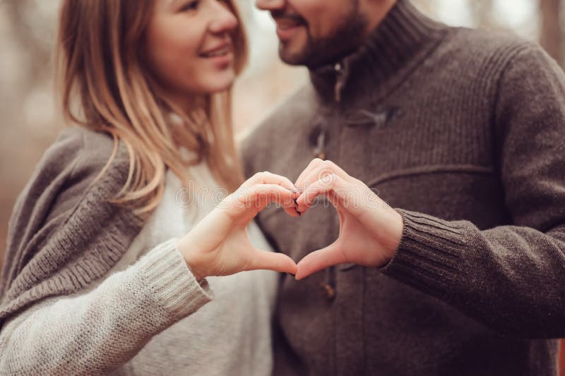 Young happy loving couple showing heart for valentine day on cozy outdoor walk in forest