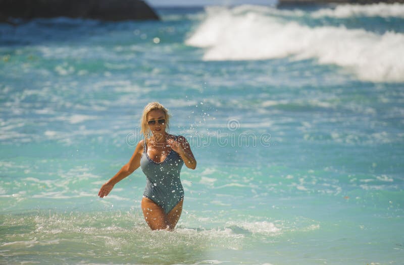 Young happy and sexy blond woman in swimsuit bikini playing with waves in the sea at stunning beautiful tropical beach enjoying