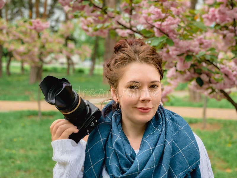 Young happy smiling red-haired woman with a white sweater and blue scarf holds in her hands and looks at the camera near