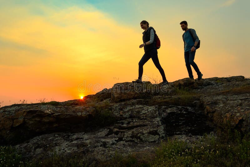 Young Happy Travelers Hiking with Backpacks on the Rocky Trail at Summer Sunset. Family Travel and Adventure Concept.