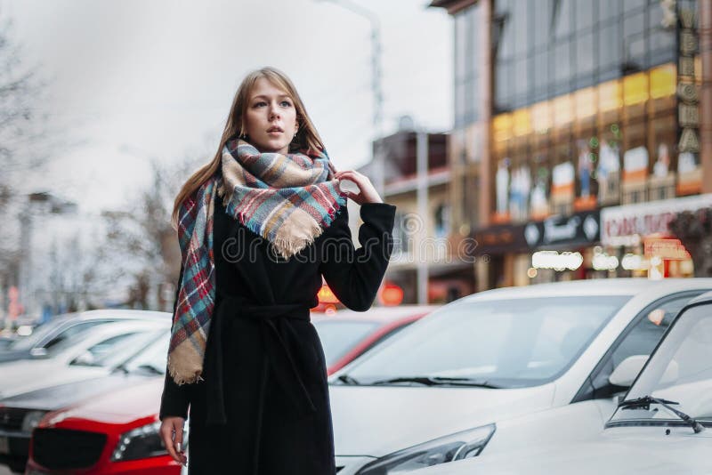 Young happy woman blonde in a black coat and scarf walks through city. Waiting for meeting stock photography Young happy woman blonde in a black coat and scarf walks through city. Waiting for meeting stock photography