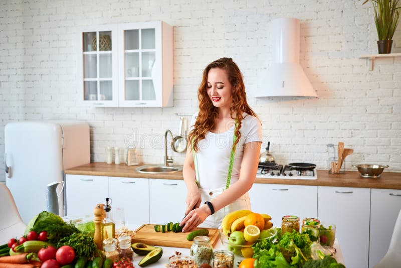 Young happy woman cutting cucumber for making salad in the beautiful kitchen with green fresh ingredients indoors. Healthy food royalty free stock photography Young happy woman cutting cucumber for making salad in the beautiful kitchen with green fresh ingredients indoors. Healthy food royalty free stock photography