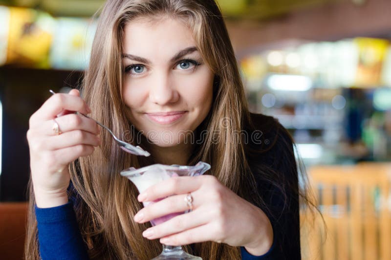 Young happy woman eating ice cream in cafe