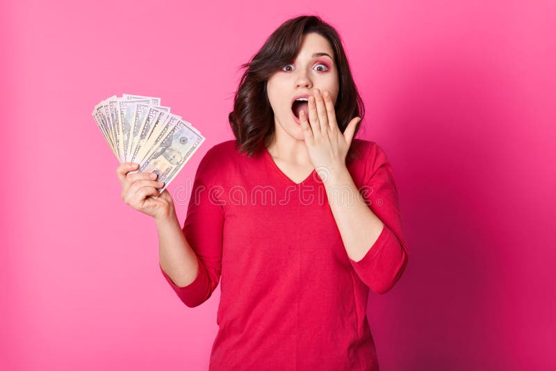 Young happy woman with money in hand, with opened mouth, looks surprised. Brunette girl wins in lottery. Lucky female dressed red stock photography Young happy woman with money in hand, with opened mouth, looks surprised. Brunette girl wins in lottery. Lucky female dressed red stock photography